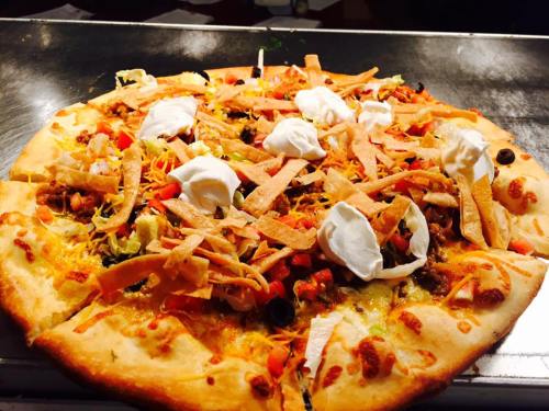 A freshly baked pizza topped with ground beef, cheese, lettuce, tomatoes, olives, tortilla strips, and dollops of sour cream.