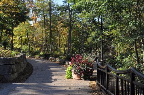 A winding path through a lush, green park with colorful flowers and trees in autumn foliage.