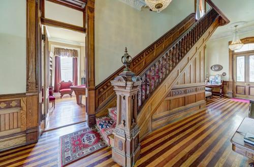 A grand wooden staircase with intricate details, leading to a well-lit room with elegant furnishings and rich wooden floors.