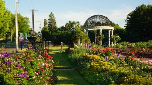 A vibrant garden path lined with colorful flowers leads to a decorative gazebo under a clear blue sky.