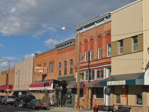 Historic brick buildings line a street, featuring shops, a bar, and a casino under a partly cloudy sky.