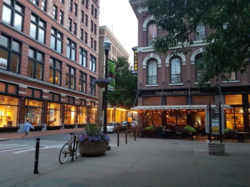 A street scene at dusk featuring Tupelo Honey Cafe, with outdoor seating, shops, and a bicycle parked nearby.