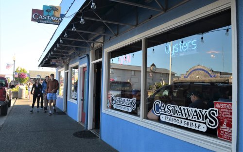 Exterior of Castaways Seafood Grille with people outside, featuring large windows and an "Open" sign.
