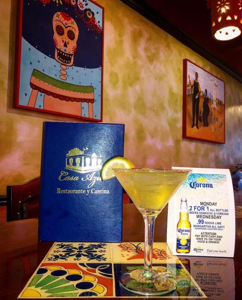 A margarita on a table with a menu and promotional flyer in a colorful restaurant setting.
