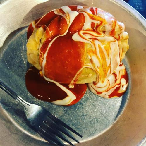 A baked pastry drizzled with red sauce and white cream, served on a metal plate with a fork.