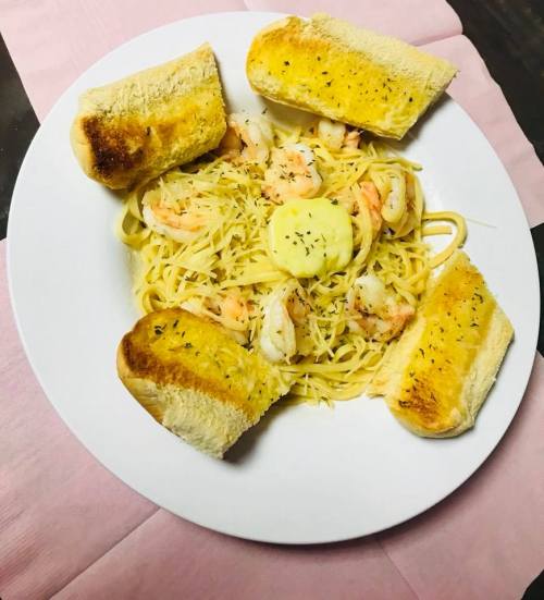A plate of shrimp pasta topped with butter and served with toasted bread on the side.