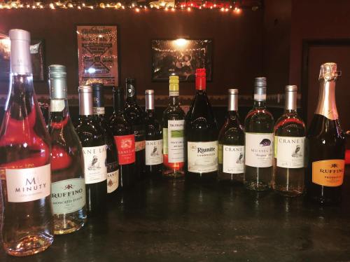 A variety of wine bottles arranged on a bar, with colorful lights in the background.