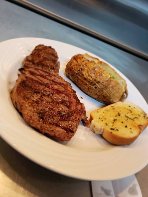 A plate with a grilled steak, a baked potato, and a slice of garlic bread.