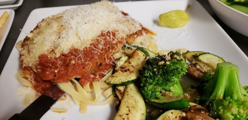 A plate of pasta with marinara sauce and cheese, served with sautéed zucchini and broccoli on the side.