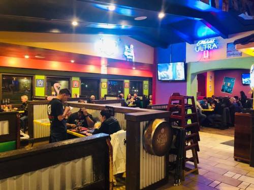 A lively restaurant interior with diners at tables, colorful decor, and a bartender serving drinks.