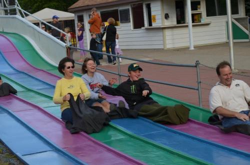 A group of four people joyfully sliding down a colorful slide at an amusement park.