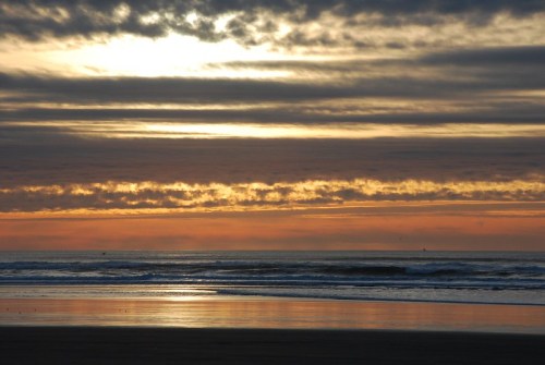A serene beach at sunset, with colorful clouds reflecting on the water and gentle waves lapping at the shore.