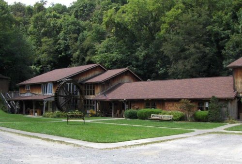A rustic wooden building surrounded by greenery, featuring a large water wheel and a sign for "Lost River Caverns."