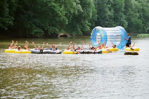 A group of people on yellow inner tubes in a river, enjoying a sunny day, with a large inflatable water ball nearby.