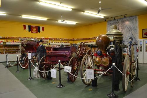 Historic fire engines displayed in a museum, surrounded by various collectibles and a yellow wall backdrop.