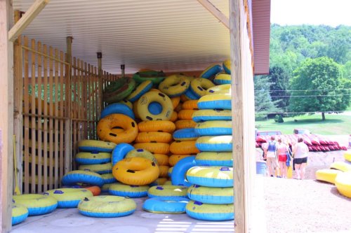 A storage area filled with stacked yellow and blue inner tubes, with people in the background preparing for water activities.