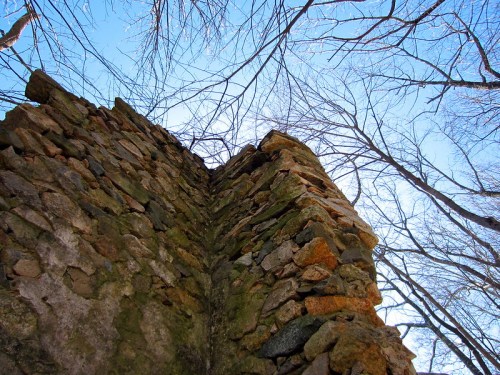 A close-up view of a stone wall corner, with bare tree branches and a clear blue sky in the background.