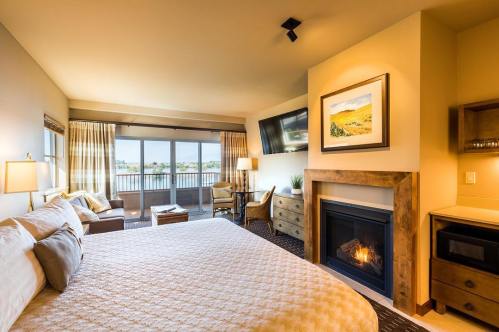 Cozy hotel room with a king bed, fireplace, seating area, and large windows offering a view. Warm, inviting decor.
