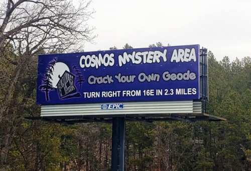 Billboard for Cosmos Mystery Area promoting geode cracking, with directions to turn right in 2.3 miles.