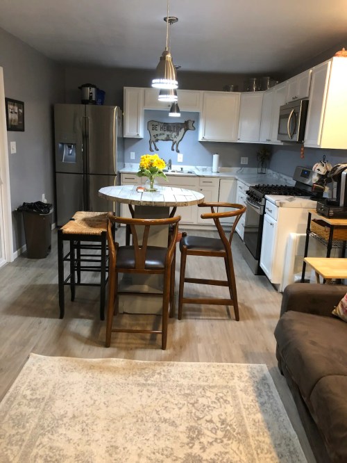 A modern kitchen with white cabinets, a round table, bar stools, and a cozy seating area. Bright and inviting atmosphere.