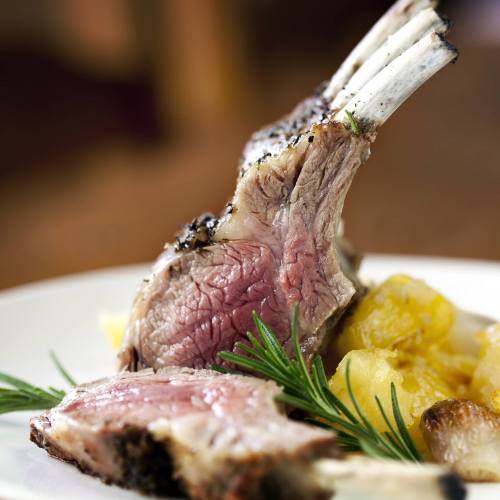 A close-up of a perfectly cooked rack of lamb with a side of roasted potatoes and garnished with rosemary.