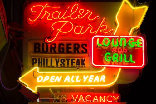 Bright neon sign for "Trailer Park" featuring "Burgers," "Philly Steak," and "Lounge & Grill," with an arrow and "Open All Year."