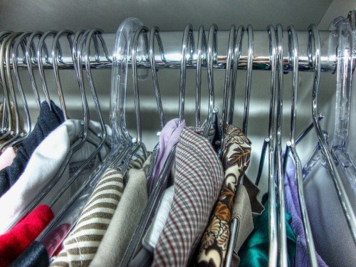 A close-up of a clothing rack with various shirts and blouses hanging on shiny metal hangers.