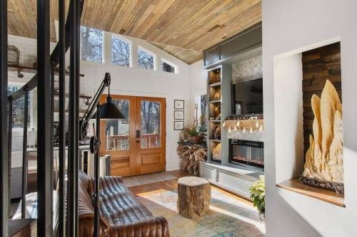 Cozy living room with a wooden ceiling, leather sofa, fireplace, and large windows letting in natural light.