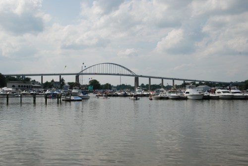 A view of a busy marina with boats and a large bridge in the background under a cloudy sky.