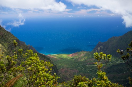 A panoramic view of lush green mountains descending to a vibrant blue ocean under a partly cloudy sky.