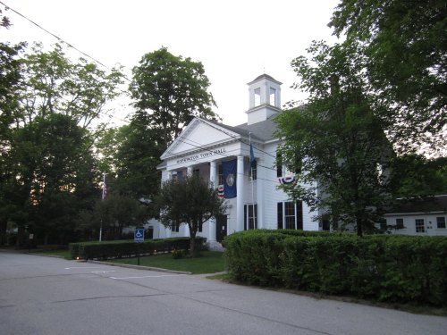 Historic town hall building surrounded by trees, with flags and decorative bunting, on a quiet street.