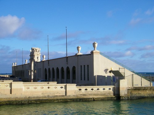 Historic building by the water with arched windows and decorative elements, under a blue sky with scattered clouds.
