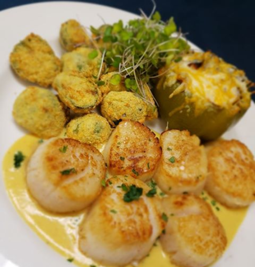 A plate featuring seared scallops, stuffed green pepper, and baked clams, garnished with microgreens.