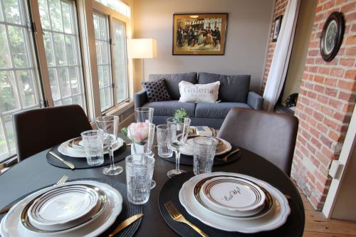 A dining table set with elegant plates and glasses, with a cozy living area featuring a sofa in the background.