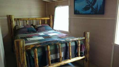 Cozy bedroom featuring a log bed with a patchwork quilt and a nature-themed wall art. Natural light from a window.