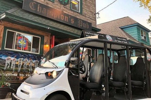 A small electric shuttle parked outside Champion's Pub, with a colorful sign and a cozy building in the background.