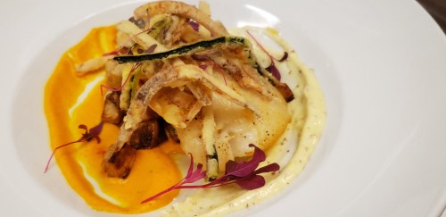 A beautifully plated dish featuring fried vegetables, a piece of fish, and colorful sauces on a white plate.
