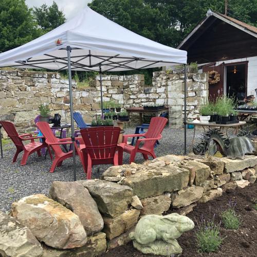 A cozy outdoor seating area with red chairs under a white canopy, surrounded by stone walls and greenery.