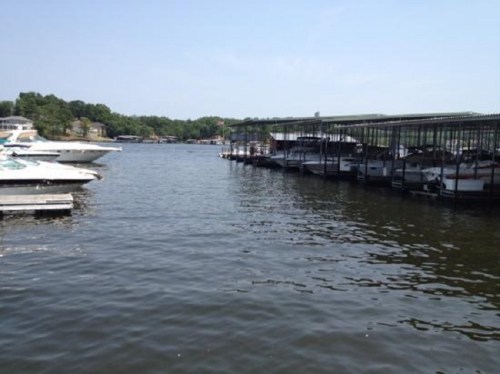 A calm lake scene with boats docked at a marina under clear blue skies.