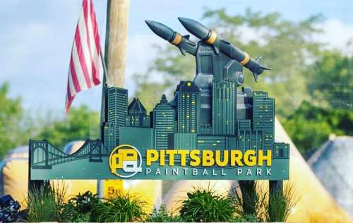 Sign for Pittsburgh Paintball Park featuring city skyline and missile sculptures, with an American flag in the background.