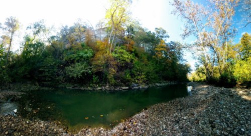 A serene river scene surrounded by lush trees and rocky banks, with autumn colors reflecting in the water.