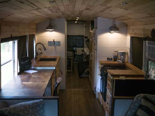 Interior of a cozy, converted bus featuring wooden accents, a kitchen area, and a living space with natural light.