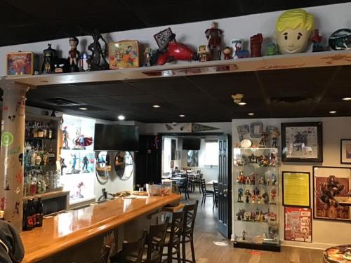 A cozy bar with a wooden counter, shelves of collectibles, and a dining area in a vibrant, themed decor.