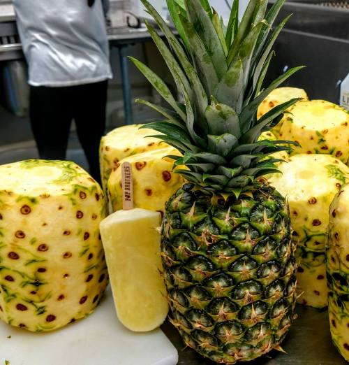 A whole pineapple surrounded by peeled pineapple halves and a cut piece on a kitchen counter.
