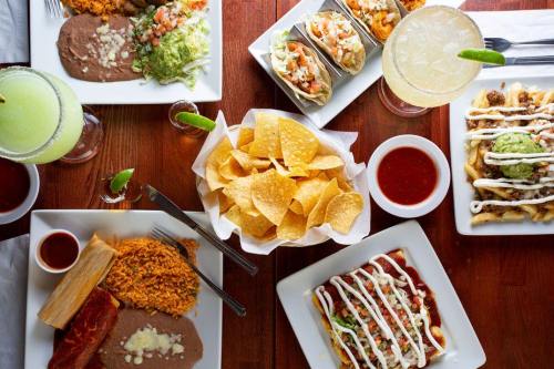A vibrant spread of Mexican dishes including tacos, rice, beans, chips, and drinks on a wooden table.