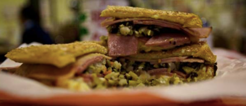 A close-up of a stacked sandwich filled with layers of ham, pickles, and mustard, served on a plate.