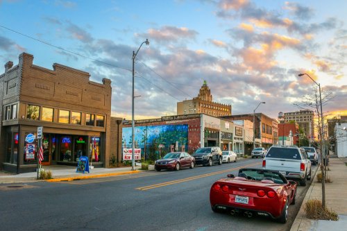 A vibrant street scene at sunset, featuring shops, parked cars, and a colorful mural on a building.