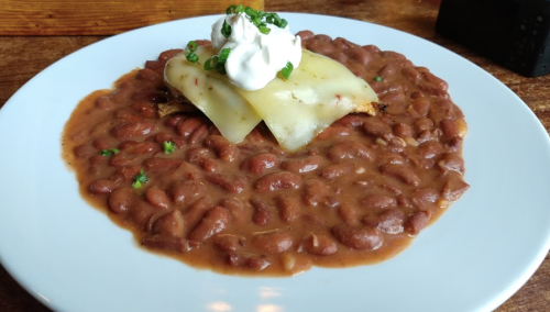 A plate of creamy refried beans topped with melted cheese, a dollop of sour cream, and green onions.