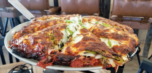 A golden-brown, cheesy pizza topped with green peppers and onions, served on a round metal tray.