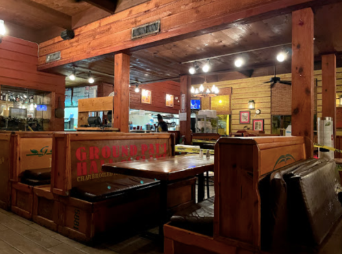 Cozy restaurant interior with wooden decor, tables, and a visible kitchen area in the background. Warm lighting.